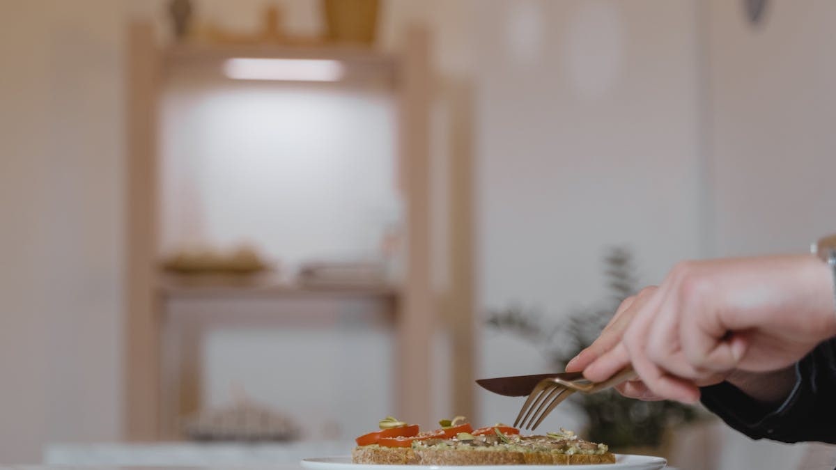 A hand slicing vegan sandwich on a ceramic plate with focus on healthy lifestyle.